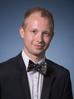 The image features a young man dressed in formal attire with a bow tie, posing for a portrait against a blue background.