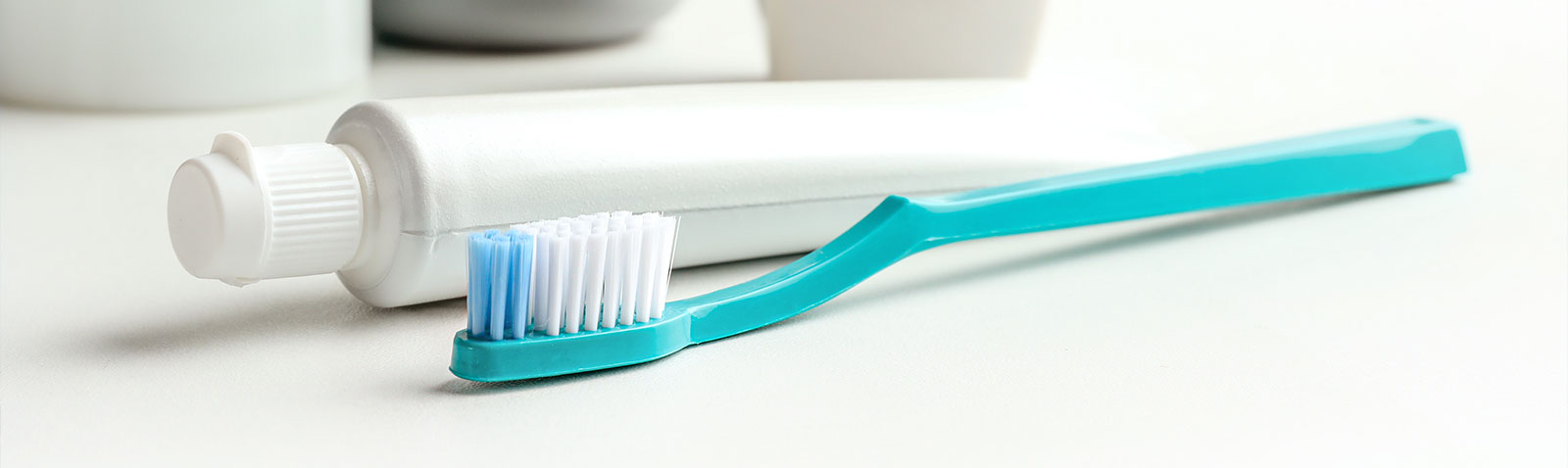 Toothbrush with blue bristles resting on a white surface next to a white cup.