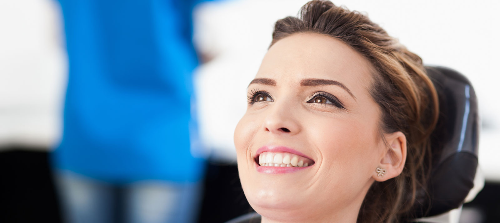 The image shows a woman with a smiling expression, wearing glasses and sitting in a wheelchair, with a blurred background suggesting an indoor setting.