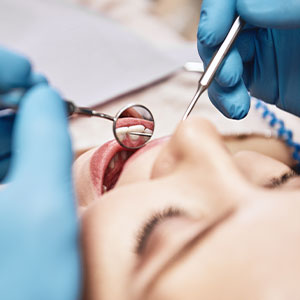 The image shows a person receiving dental care with a dentist using dental tools on their teeth, while another person appears to be observing or assisting.